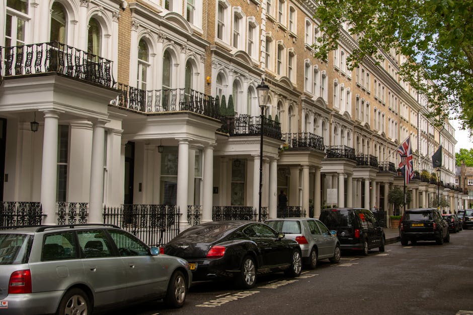 A row of traditional Victorian terraced houses with ornate ironwork balconies and bay windows, situated on a slightly elevated street level with a brick retaining wall and steps leading up to each ent