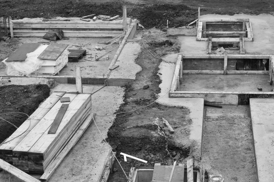 The image depicts a construction site during early foundation work, featuring multiple rectangular wooden forms set into a concrete base, likely for future structural elements such as walls or columns
